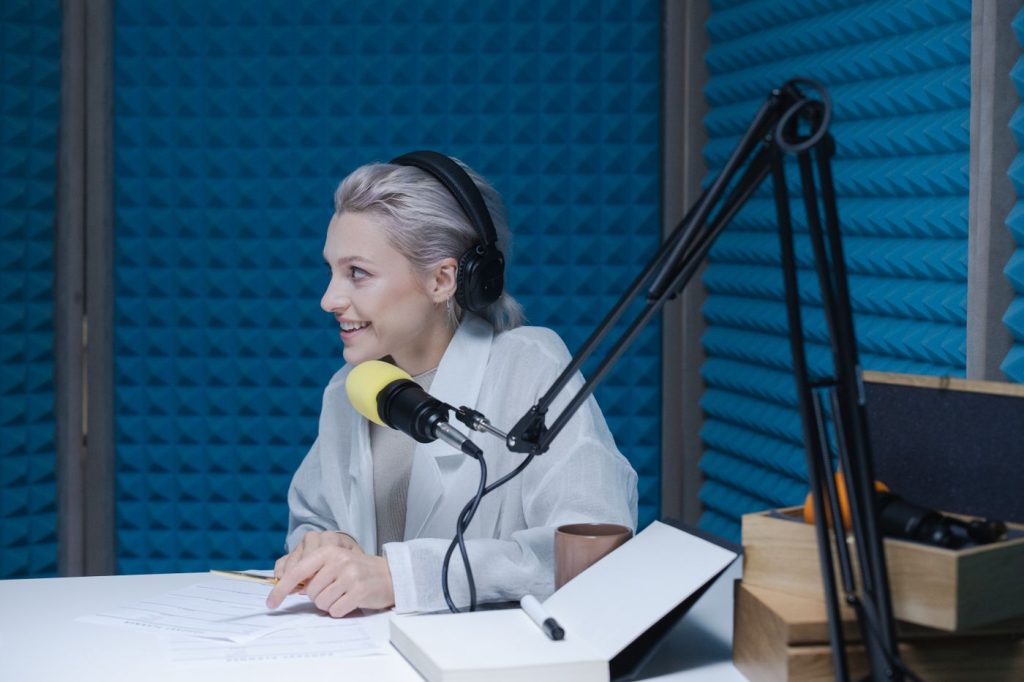Woman in headphones recording voice-over content beside a microphone in a soundproofed studio