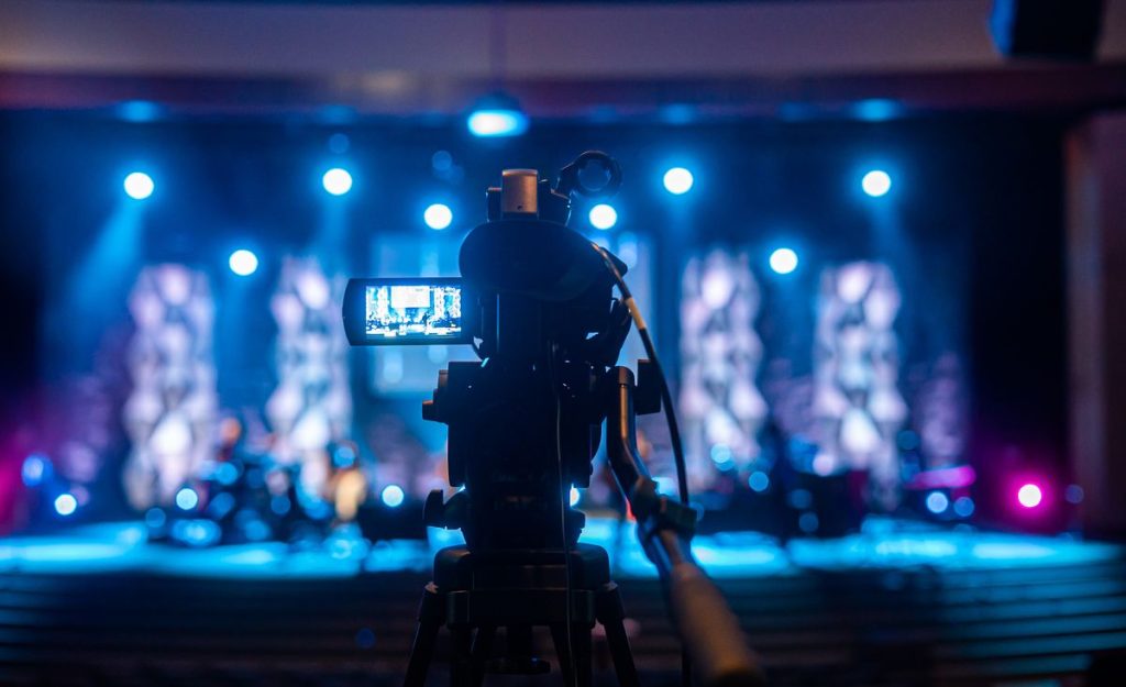 Professional video camera filming an illuminated stage during a live event